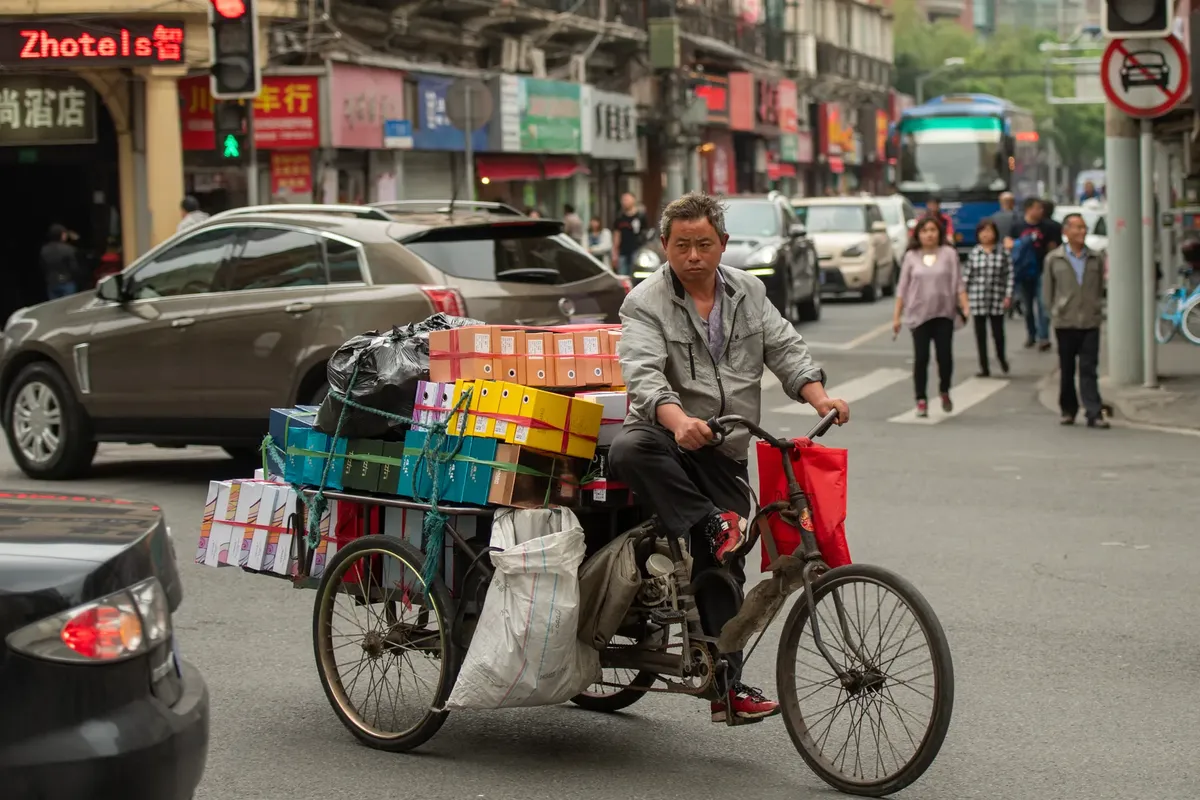 A man transporting goods on a tricycle in a bustling Shanghai street, showcasing urban life and local commerce.