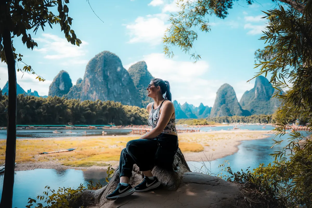 A woman sitting on a rock, admiring the stunning karst landscape of Guilin, China.