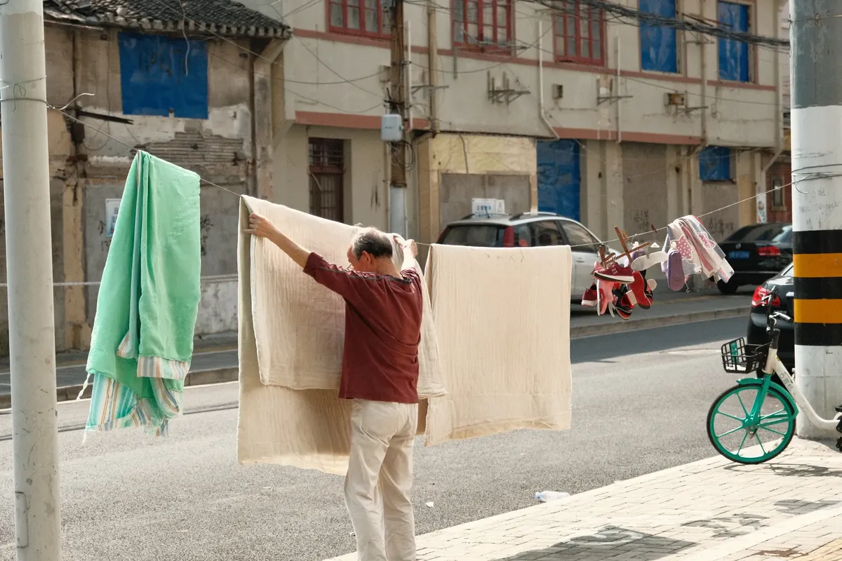 A man hangs laundry on a street in Shanghai, capturing everyday life and urban culture.