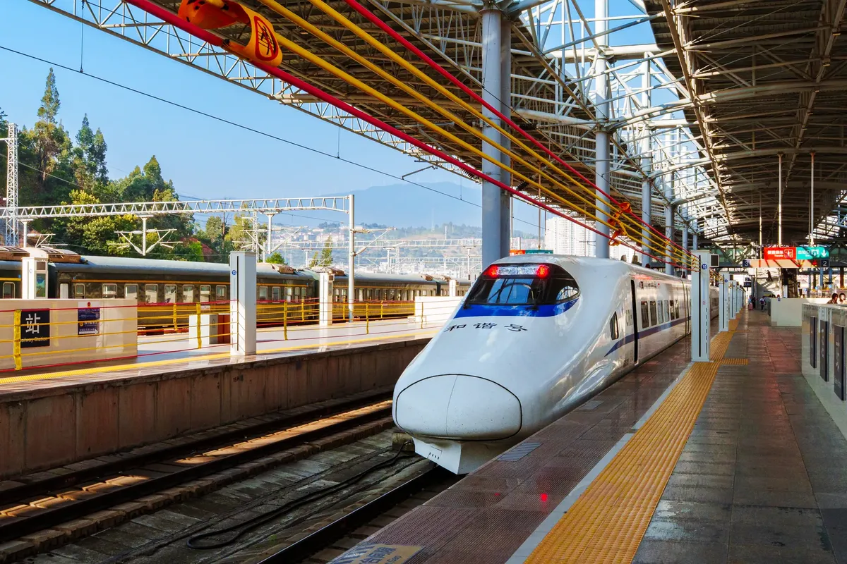 High-speed bullet train at a busy outdoor city station, sunny day.