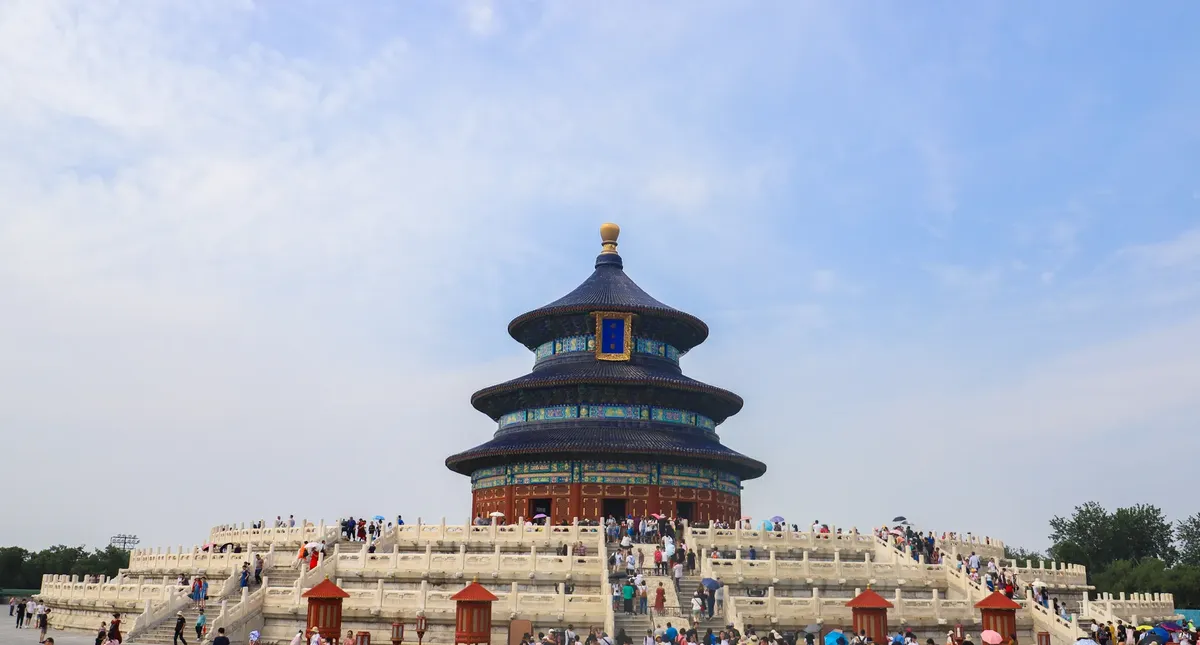 The majestic Temple of Heaven in Beijing with a lively crowd under a clear blue sky.